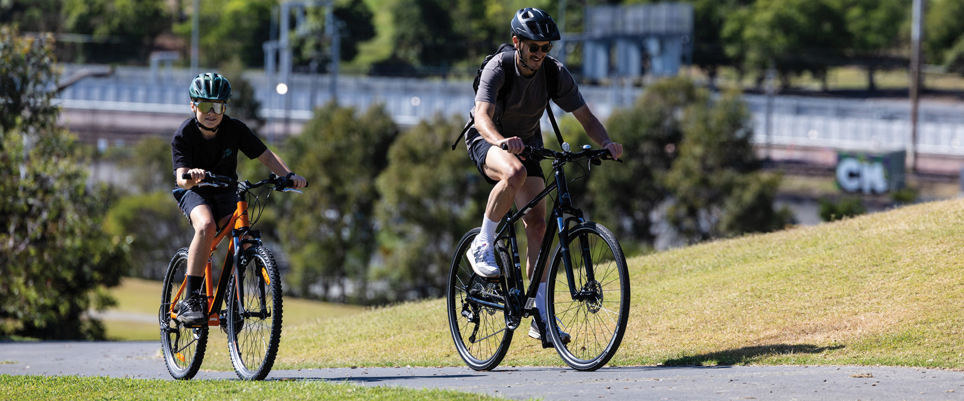 Two cyclists riding MERIDA mountain and commuter bikes across the bike path on a sunny day. MERIDA Matts 6.5v and MERIDA Speeder.